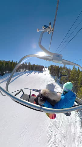 Young snowboarders ride the chairlift and observe the scenic nature on a sunny winter day. Man and woman on a snowboarding vacation in Colorado relax during the chair lift ride to top of the mountain.