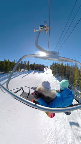 Young snowboarders ride the chairlift and observe the scenic nature on a sunny winter day. Man and woman on a snowboarding vacation in Colorado relax during the chair lift ride to top of the mountain.