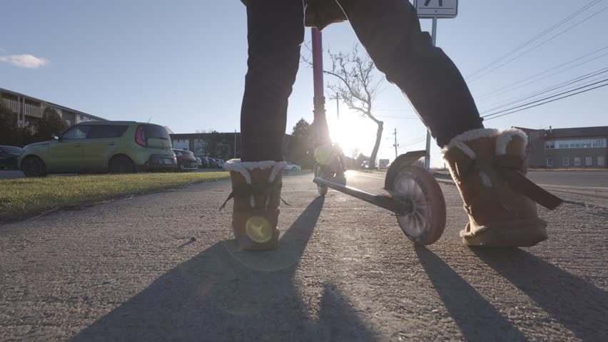 A Young Girl Glides Along The Sidewalk On Her Scooter, The Setting Sun Casting A Warm Glow. Slow Motion Captures Every Detail Of Her Joyful Ride In The City Outdoors.