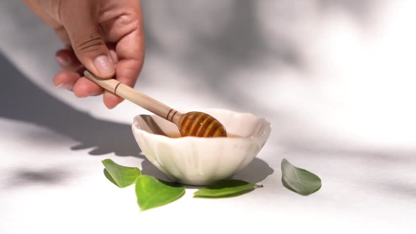 A person using a honey dipper to drizzle golden honey into a bowl, showcasing the smooth and sweet texture of the honey