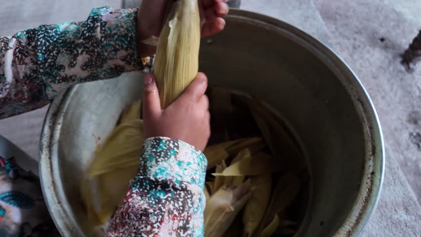 Preparing traditional dish with corn husks and hands in local kitchen setting
