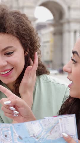 Vertical video. Young happy beautiful girls looking for direction at city map while enjoying vacation in Lisbon, Portugal, Europe. Holiday lifestyle and friendship concept.