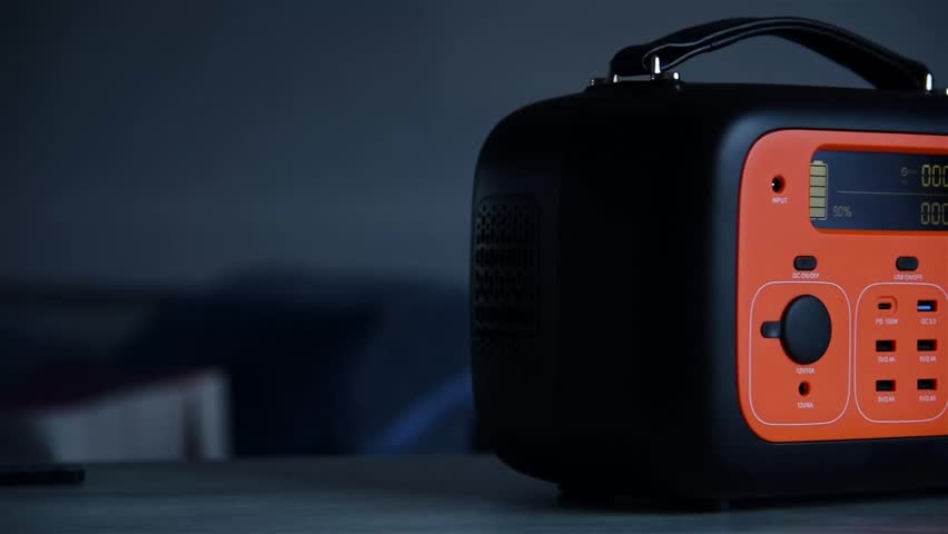 Close-up of a portable power station with cables connected, bright orange panel, on a table indoors, concept of backup energy. Slow Motion Effect.