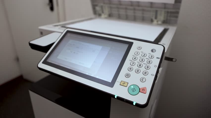 An office worker scans an A3 sheet of paper on a scanner. A man's hand presses a button to scan or copy a document on an office MFP.