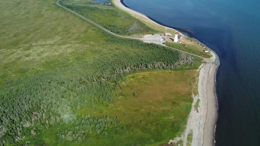High altitude aerial view capturing the picturesque lighthouse of Miscou Island near a lush forest, peat bog and a sandy beach animated by the waves of the Gulf of St. Lawrence. New Brunswick, Canada.
