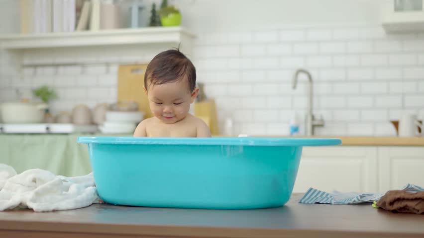 Asian baby taking a bath in a blue tub at home