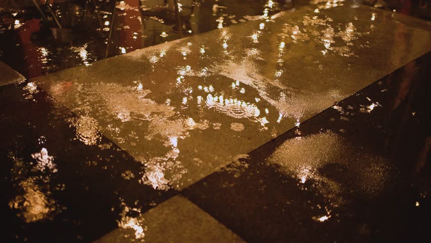 Yellow lights of the coffee shop reflecting from the wet ground during the rain. Illuminated city on a dark rainy night.