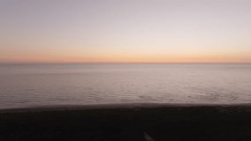 Calm ocean waves with an orange and pink sunset sky meeting the horizon viewed from a green shore - Powered by Shutterstock - Get 15% off with code: PIKWIZARD15