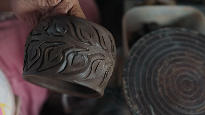 Close up hands of unknown master holding raw ceramic cup and turning around while covering with clear varnish. Kitchen utensil with floral pattern going through preparing for baking process.