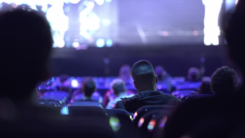 A movie theater full with diverse audience watching an exciting movie back view