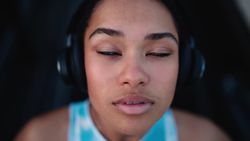 Close-up of young African American woman wearing headphones, looking upward with thoughtful expression. Immersed in sound and contemplation, showcasing beauty, focus, individuality in modern context