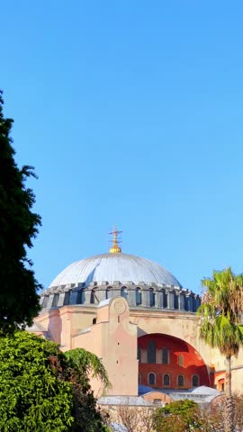 ISTANBUL, TURKEY - JULY 15, 2024: The beautiful Hagia Sophia and the fountain with trees and flower beds in the park. The Christian Patriarchal Basilica, the Imperial Mosque against the blue sky. 4K