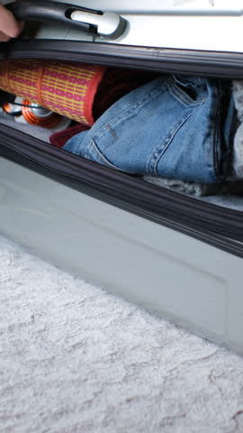 Vertical video. Close-up of a woman zipping up a suitcase filled with neatly packed clothes, preparing for her upcoming adventure and travels