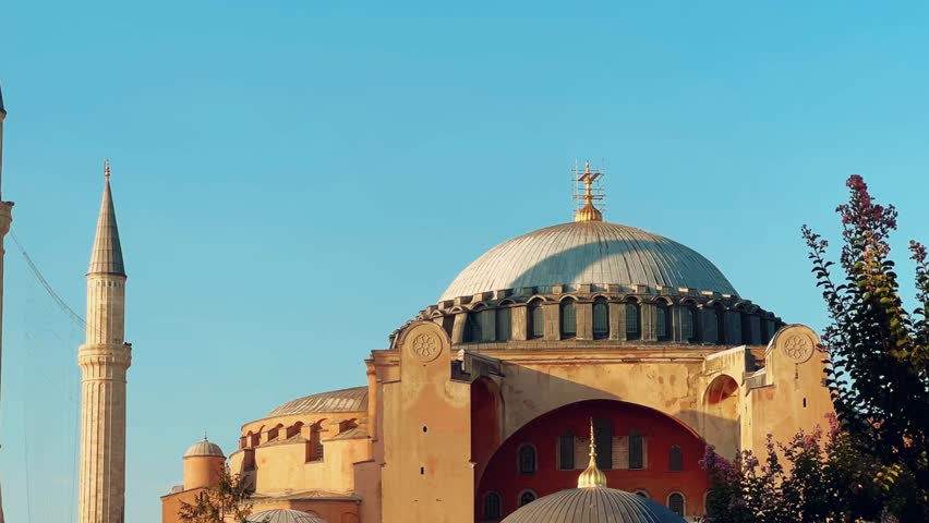 ISTANBUL, TURKEY - JULY 15, 2024: The beautiful Hagia Sophia and the fountain with trees and flower beds in the park. The Christian Patriarchal Basilica, the Imperial Mosque against the blue sky. 4K