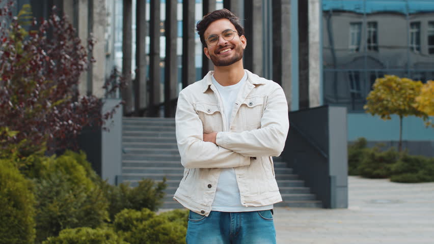 Portrait of happy young Indian man smiling friendly, glad expression looking at camera dreaming, resting relaxation feel satisfied good news outdoors. Arabian Hindu guy in city street. Business people