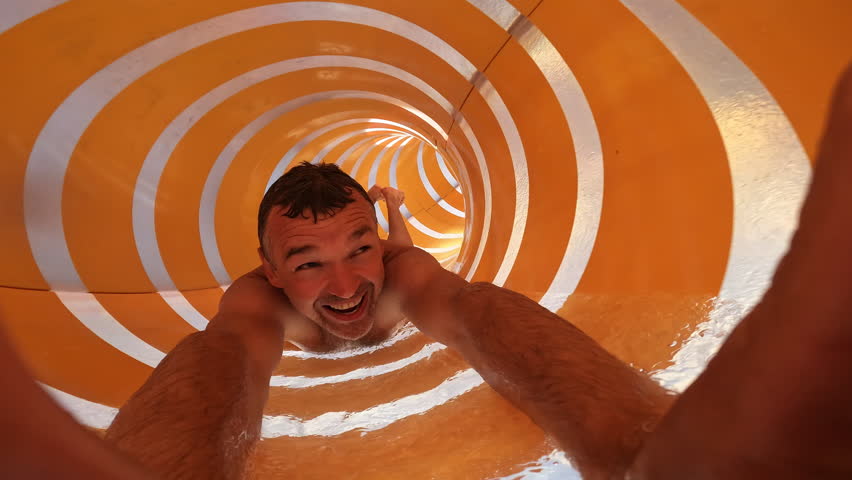 Man enjoys sliding down a twisting yellow waterslide, radiating happiness and excitement in a fun filled waterpark setting