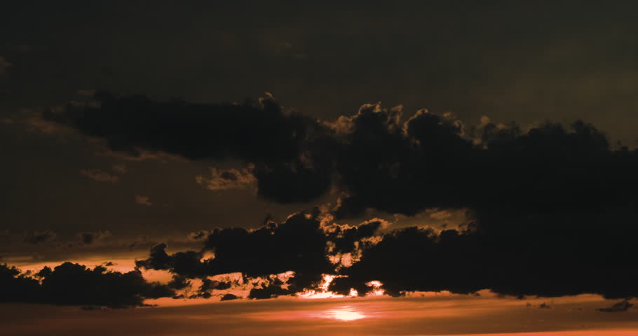 Timelapse close-up of orange and dark sunset sky with sun hidden behing moving contrasting black clouds