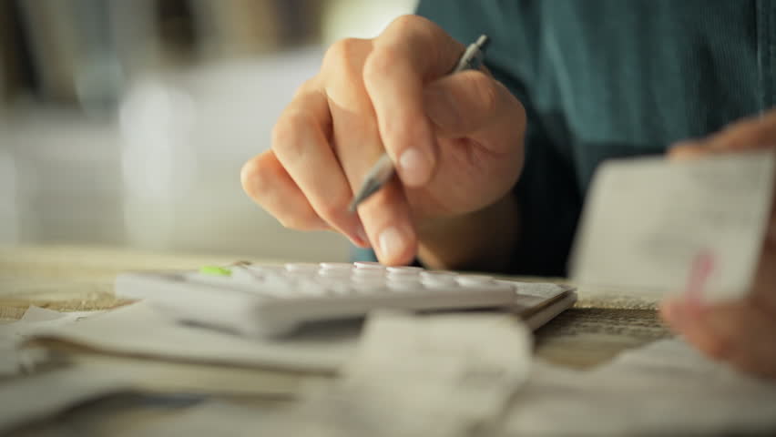 Hands engaged in reviewing receipts and using a calculator. Focus is on budgeting and tracking expenses in a cozy home environment, emphasizing financial responsibility after work hours