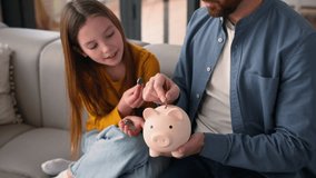 Happy Caucasian family little schoolgirl child girl daughter kid saving money at home guy parent dad male father man put coins in piggy bank savings economy financial education invest charity donation - Powered by Shutterstock - Get 15% off with code: PIKWIZARD15