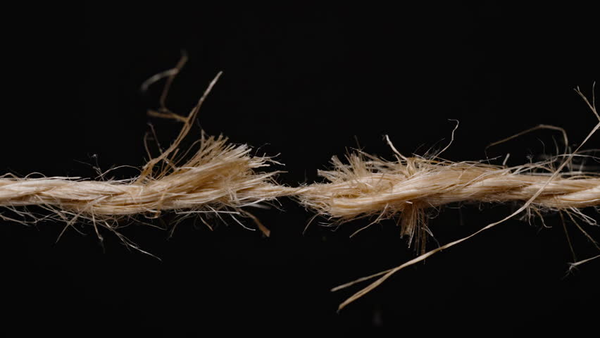 Close-up of a frayed rope on the verge of snapping, showing tension and stress in the fibers against a black background. jute or hemp rope