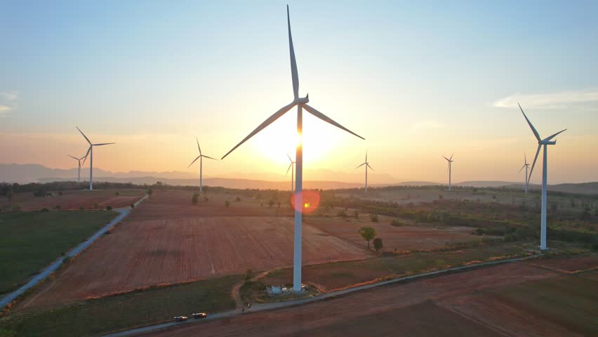 Aerial drone shot flying outdoors above the wind turbine field view. Landscape of the windmill power turbines farm generating clean renewable energy for sustainable development in rural area at sunset