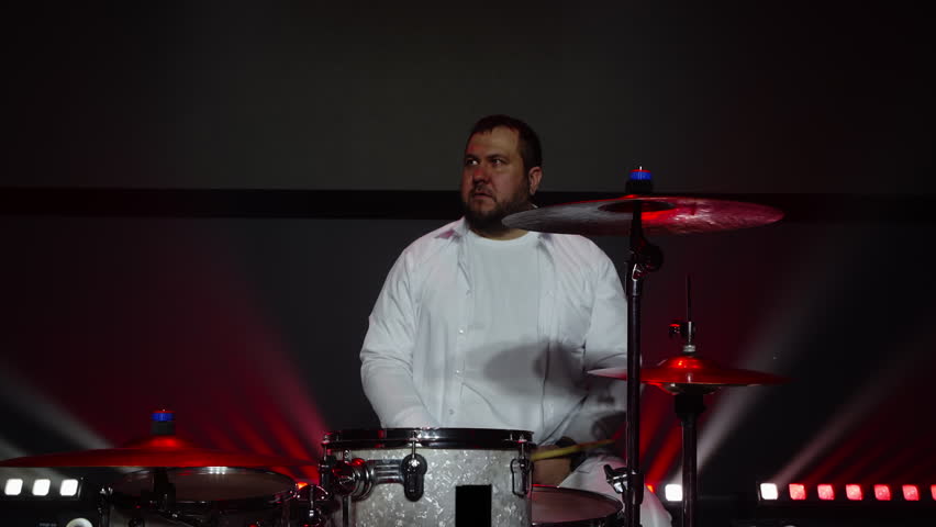 Talented drummer playing music on drumset. Man is performing with percussion instruments on illuminated stage. He is enjoying in show at event.