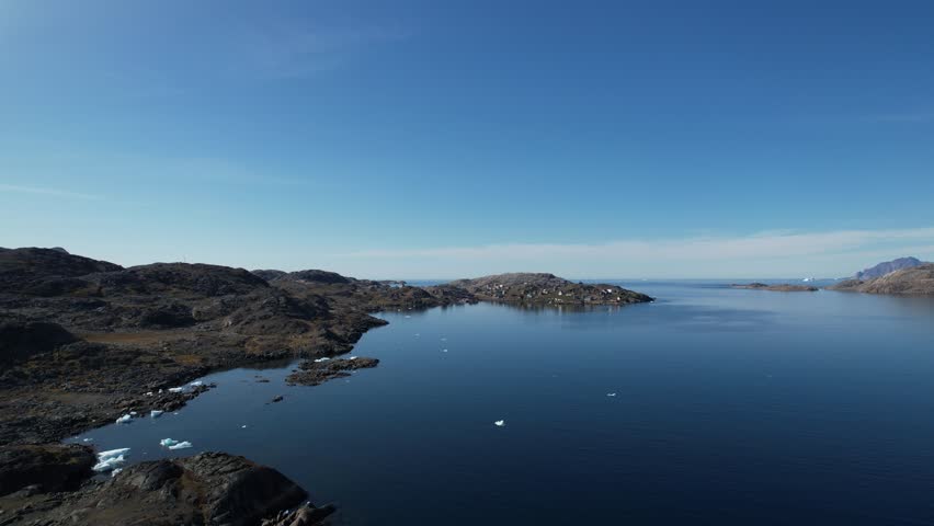 A Greenlandic landscape filmed from above, with a typical small Inuit village (settlement) in the background. Filmed in Greenland during the summer on a sunny day.