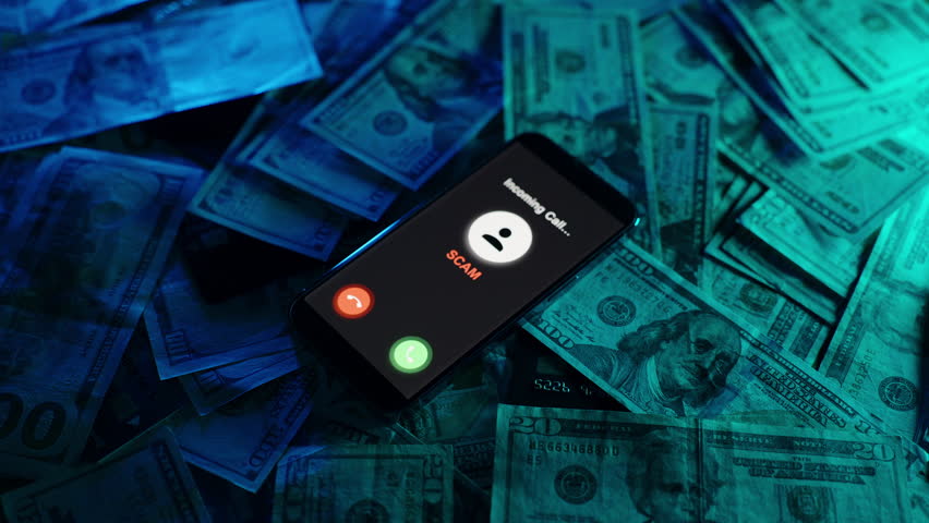 A smartphone displays a scam alert with incoming call icons glowing against a background of scattered US dollar bills, captured in a moody, low-light setting.