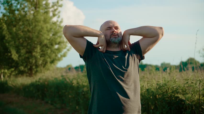 Relaxed male stretching and rolling shoulders to relieve fatigue and tension. Calm man focusing on gentle shoulder exercises to release stress and improve posture. Mindful guy engaging in soothing