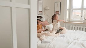 Two young girls relax on a bed, one engrossed in a virtual reality headset and controllers, while the other looks on, holding a tablet. - Powered by Shutterstock - Get 15% off with code: PIKWIZARD15