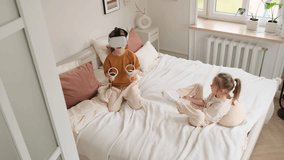 High-angle view of two children on a bed. One child is immersed in a virtual reality experience, wearing a VR headset and holding controllers. The other child sits nearby, observing. - Powered by Shutterstock - Get 15% off with code: PIKWIZARD15