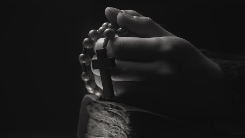 Hands folded in prayer on a Holy Bible in church. Woman praying with a wooden cross. Spirituality religion and hope concept. Supplication believe and faith. Abstract vintage religious dark background