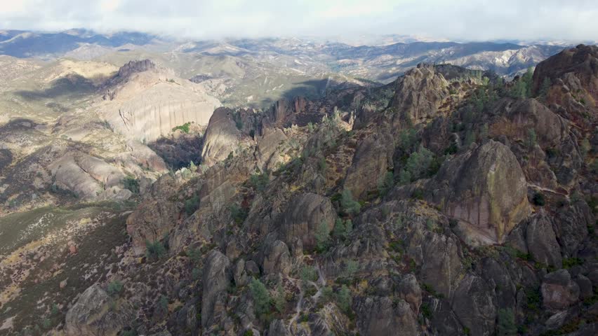 A drone view of rocky terrain landscape under a cloudy sky with sunlight in Pinnacles National Park, California, United States