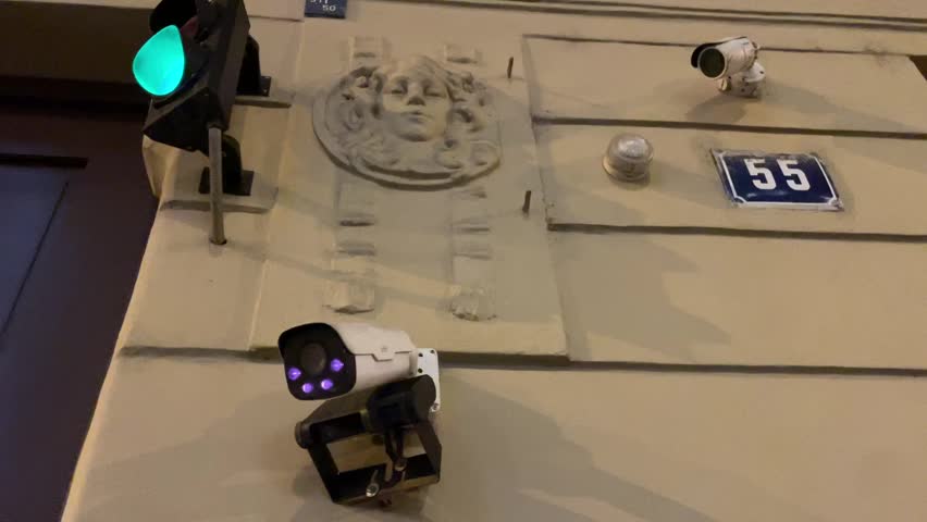 A collection of street surveillance cameras is positioned near a traffic light, mounted on wall that prominently displays a number. Urban monitoring systems, emphasizing security or traffic management