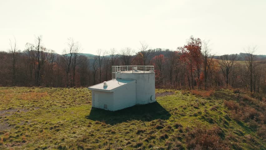 Aerial orbit around white water tank unit in an open field, surrounded by grass and trees