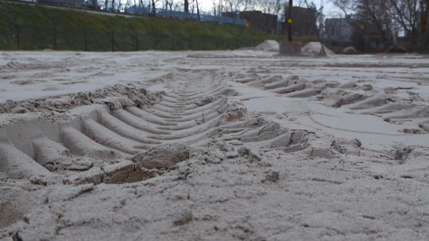 Large construction vehicle tire tracks on soft and yellow construction sand during autumn time in a cloudy day in Estonia. close up footage with a train station with trees in the background.