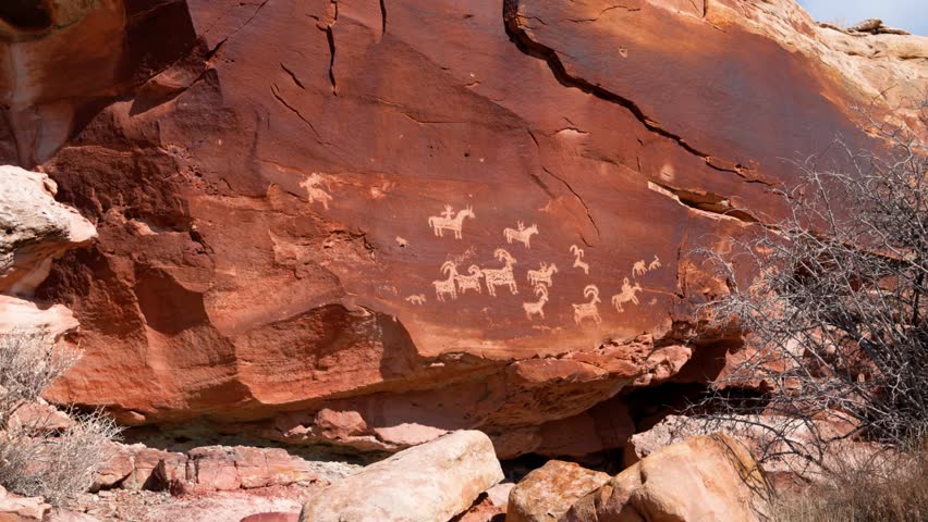 Native Carvings of goats and other wild animals in the red rock boulders of Arches National Park on a sunny day.