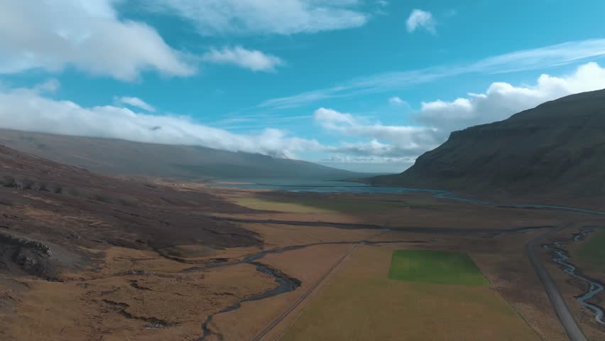 Wide valley, field, mountains, and a river flowing to an inlet sea bay in east Iceland - aerial flyover