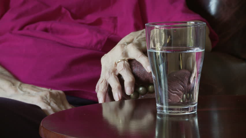 Elderly woman's hands, crippled with arthritis, pick up a glass of water to