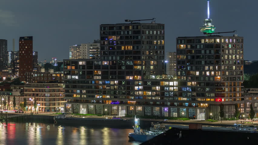 Panoramic aerial timelapse of Katendrecht peninsula at night and Maashaven harbour in Rotterdam, The Netherlands. Illuminated city skyline, modern skyscrapers and Euromast, houses on a waterfront
