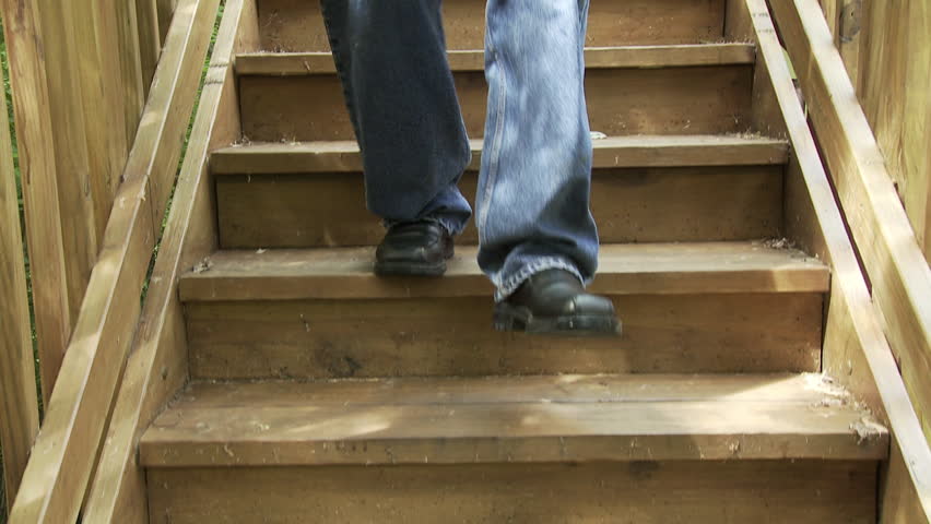 Man's legs and feet, blue jeans, black shoes, walking down a wooden staircase. 