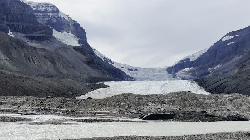 Striking view of Athabasca Glacier, part of Columbia Icefield in Jasper National Park, Alberta, Canada, with icy expanse flanked by rugged, rocky peaks under cloudy sky, Canada