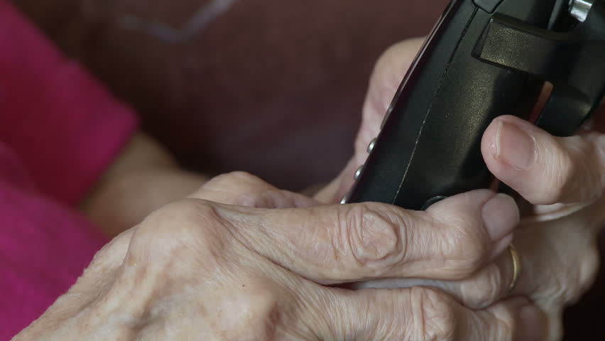 Elderly woman's hands, crippled with arthritis, dialling on a phone.