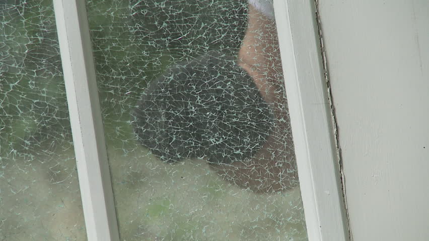 Close up on gloved fist smashing through shattered windows. Frontal view,