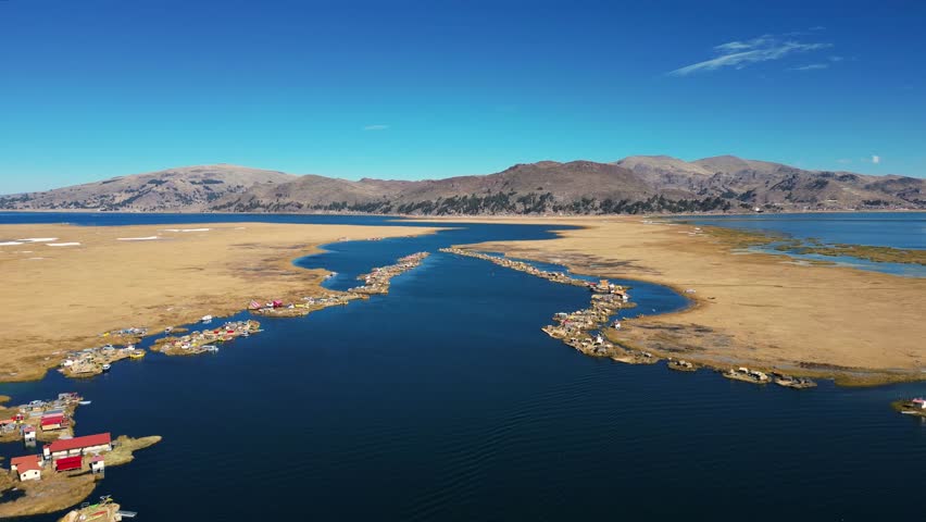 Drone footage of Lake Titicaca, Peru, showcasing floating villages, traditional boats, huts, islands, and the breathtaking Andes mountains in the background. Perfect for scenic and cultural visuals.