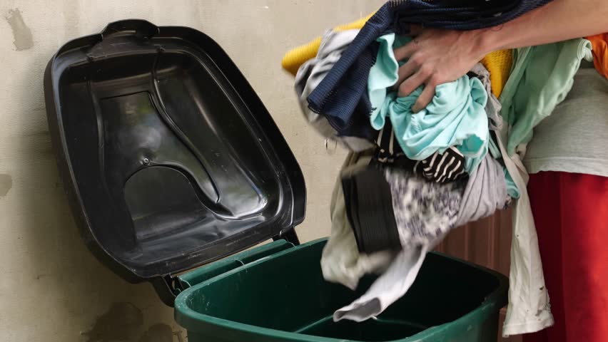 A young man throws away old clothes. Overflowing closet problem result in textile waste