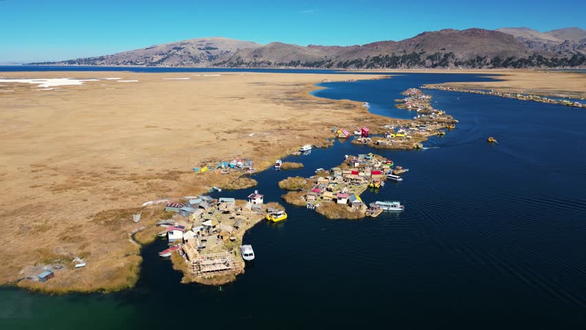 Drone footage of Lake Titicaca, Peru, showcasing floating villages, traditional boats, huts, islands, and the breathtaking Andes mountains in the background. Perfect for scenic and cultural visuals.