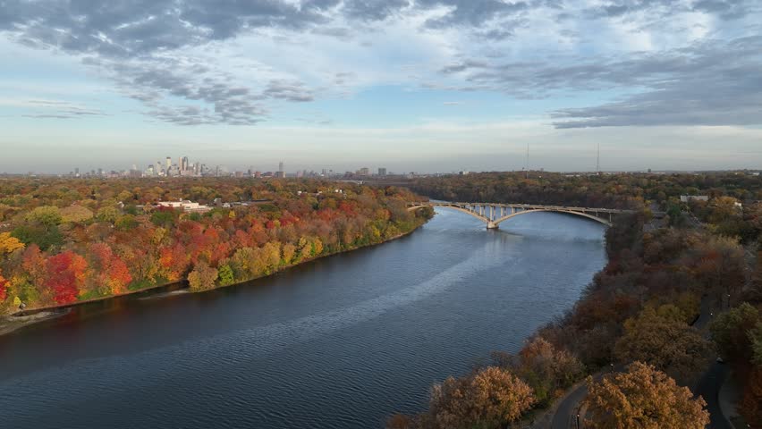 Aerial view of fall colors trees of forest beside Mississippi river with Minneapolis and St. Marshall Bridge at background in USA.