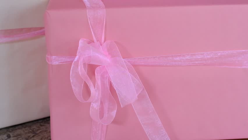 A pink box with a pink ribbon tied around it. The box is placed on a table