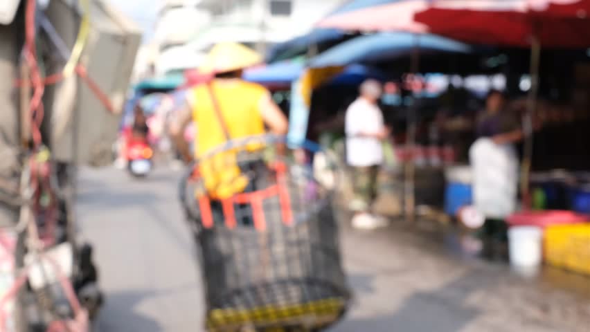 A man is riding a cart with a cage on it. The cage is full of fish. The man is wearing a yellow shirt